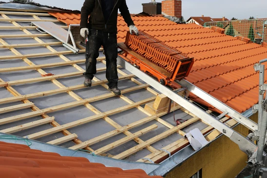Chantier de couverture en ext&eacute;rieur avec ouvrier couvreur installant des tuiles terre cuite sur toiture r&eacute;sidentielle
