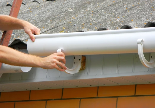 Sc&egrave;ne ext&eacute;rieure de pose de goutti&egrave;re blanche en PVC sur toiture