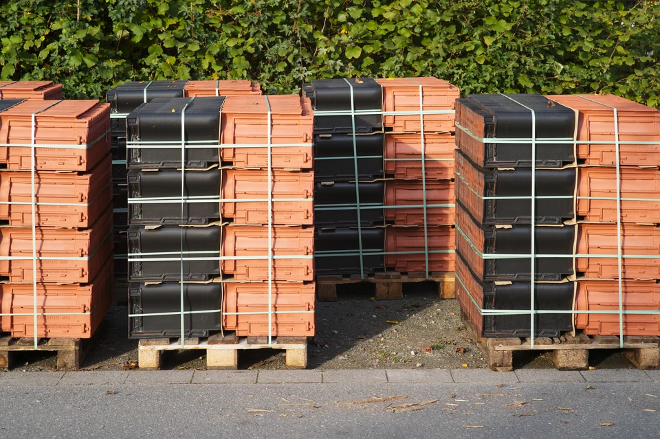 Chantier de rénovation de toiture en cours avec installation de tuiles en terre cuite brunes empilées sur charpente bois apparente