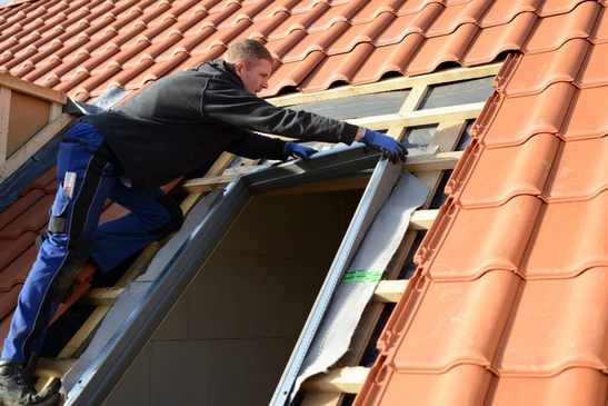 Un homme installe un film plastique de protection autour d'un ch&acirc;ssis de fen&ecirc;tre de toit Velux dans des combles en construction