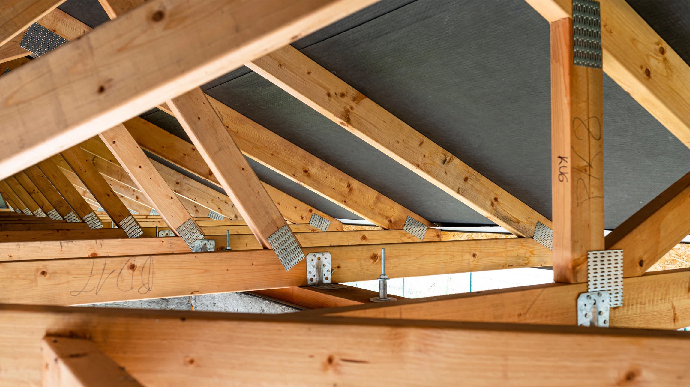 Photographie professionnelle d'un artisan ou d'une équipe de couvreurs-charpentiers effectuant un traitement de protection de charpente sur la structure en bois d'une maison. On doit voir clairement la charpente en bois, les techniciens en équipement de sécurité approprié (harnais, casque) appliquant un produit de traitement ou effectuant des opérations de maintenance de charpente en toiture. La scène doit être prise en conditions réelles de chantier, avec une perspective qui montre l'ampleur du travail et l'expertise professionnelle.
